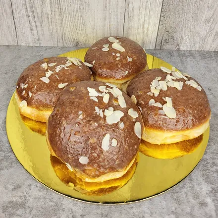 Cztery pączki w lukrze z płatkami migdałów na złotej okrągłej podkładce.