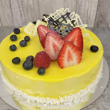 Żółty tort musowy mango-marakuja z połówkami truskawek, borówkami i czekoladową dekoracją.