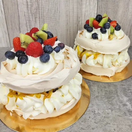 Dwa małe torty bezowe z bitą śmietaną, marakują, kiwi, truskawkami, malinami i borówkami na złotych podkładkach.