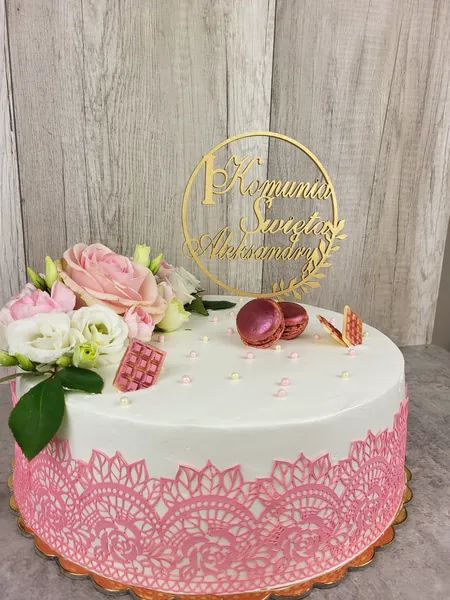 Tort komunijny z białym kremem, różową koronką cukrową na boku, różową różą, białą eustomą, makaronikami i złotym topperem, Słupno koło Radzymina